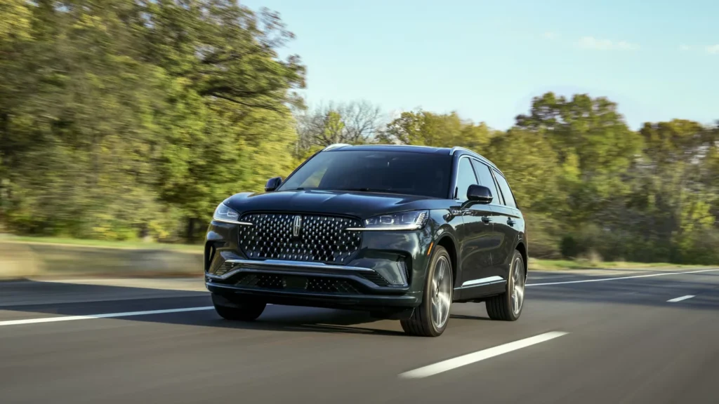 Front angle of 2025 Lincoln Aviator® Premiere in black driving on suburban road with trees.