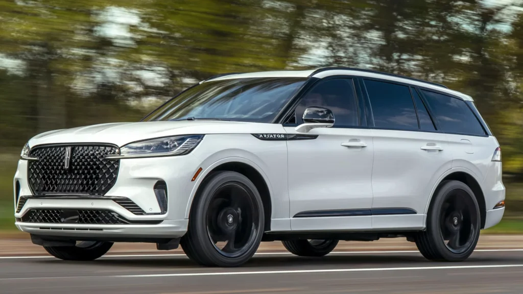 White 2025 Lincoln Aviator® SUV driving on road with motion blur and badge detail visible.