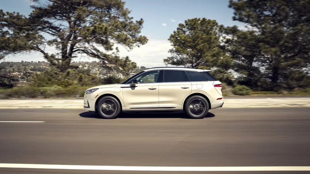 Side profile of 2025 Lincoln Corsair® in cream driving along a highway with blurred trees.