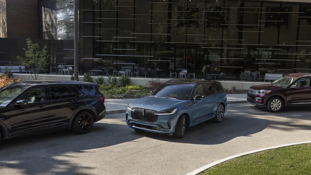 Side view of a blue 2025 Lincoln Black Label Aviator in an urban setting beside black and red SUVs.