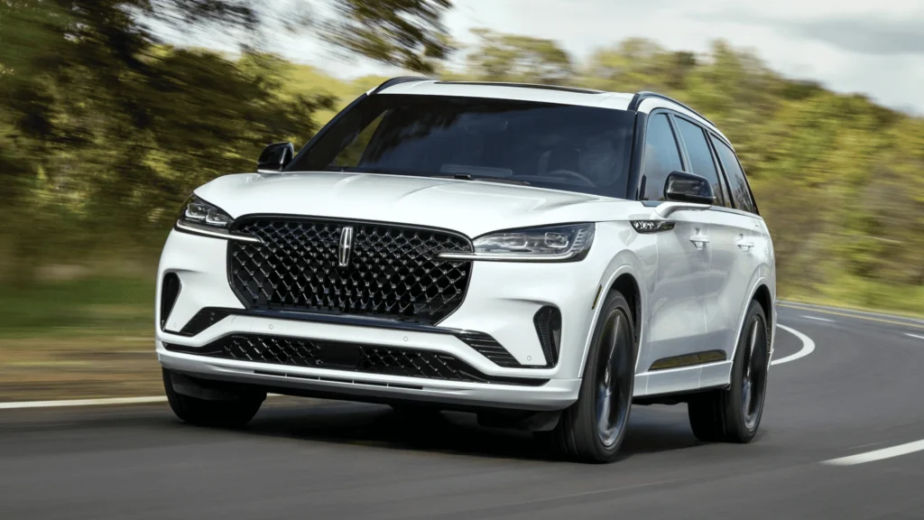 2025 Lincoln Aviator® Reserve driving on winding road with bold grille and midsize luxury SUV stance.