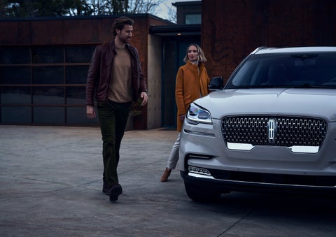 A man and a woman approaching a 2024 Lincoln Aviator® SUV, which illuminates certain lights when they are close | Nick Mayer Lincoln Westlake in Westlake OH