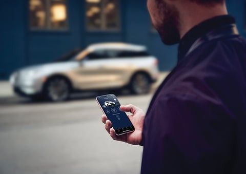 A person is shown interacting with a smartphone to connect to a Lincoln vehicle across the street. | Nick Mayer Lincoln Westlake in Westlake OH