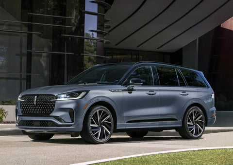 A gray 2025 Lincoln Aviator® SUV is parked outside a modern building showcasing the driver’s side of the vehicle. | Nick Mayer Lincoln Westlake in Westlake OH