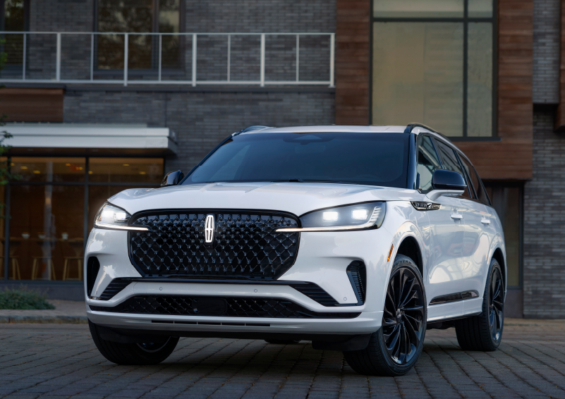 A white 2025 Lincoln Aviator® SUV is shown parked outside a modern building with gray brick and wood accents. | Nick Mayer Lincoln Westlake in Westlake OH