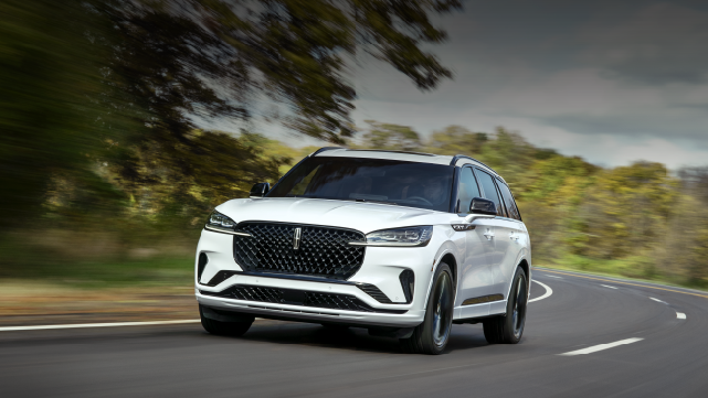 A white 2025 Lincoln Aviator® SUV is being driven down a road lined with trees. | Nick Mayer Lincoln Westlake in Westlake OH