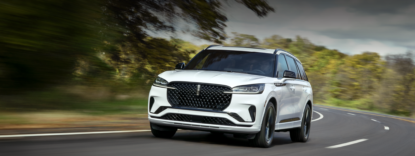 A white 2025 Lincoln Aviator® SUV is being driven down a road lined with trees. | Nick Mayer Lincoln Westlake in Westlake OH
