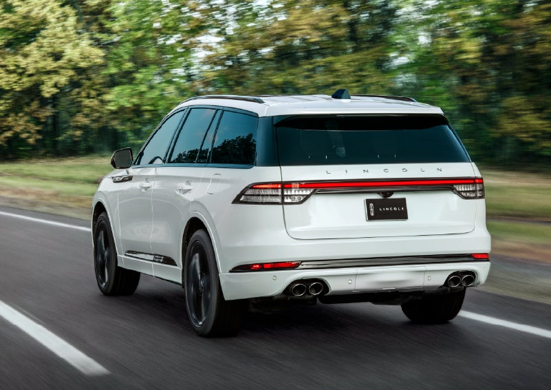 A white 2026 Lincoln Aviator® SUV is being driven away down a road lined with colorful trees. | Nick Mayer Lincoln Westlake in Westlake OH