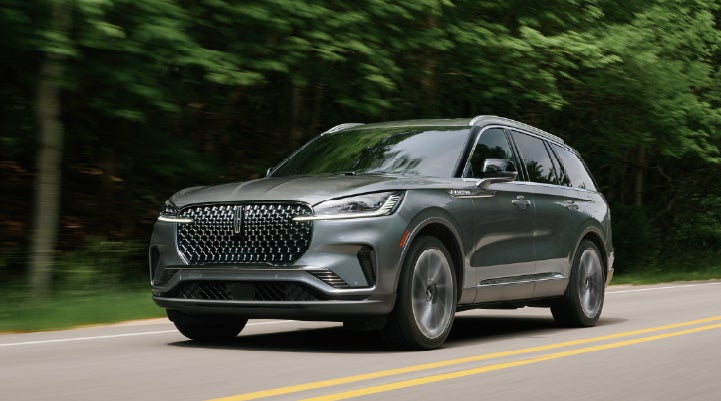 A 2027 Lincoln Aviator® SUV is being driven down a road lined with trees. | Nick Mayer Lincoln Westlake in Westlake OH