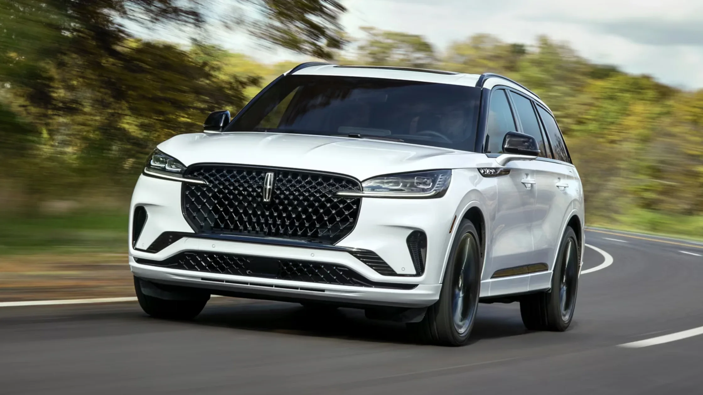 White 2025 Lincoln Aviator taking a corner, featuring sporty front fascia, LED headlights, and black accents.