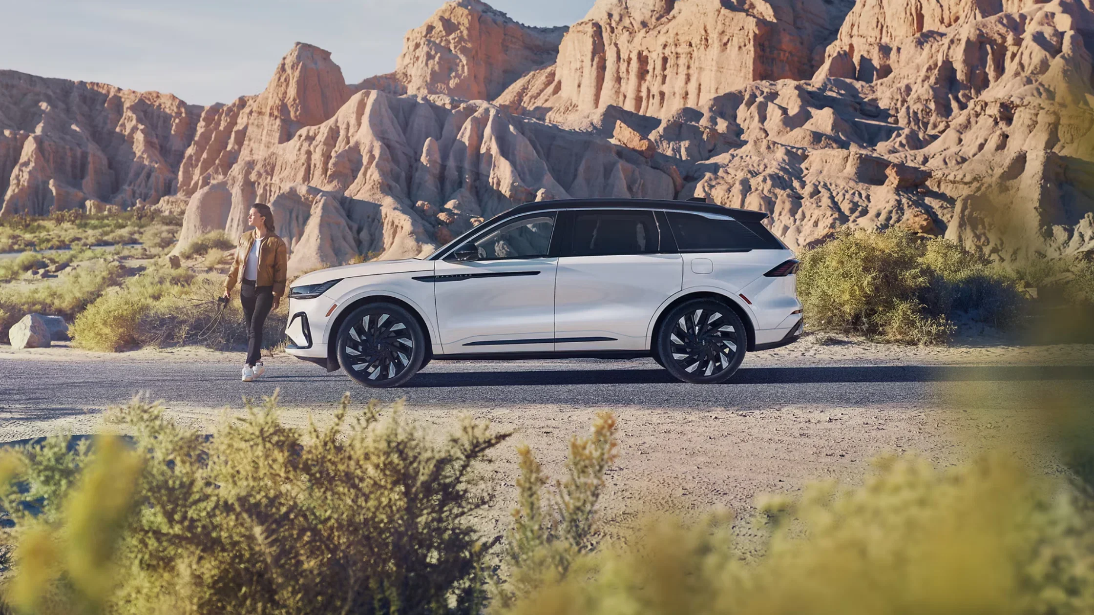 Side view of a 2025 Lincoln Black Label Nautilus® SUV parked in a desert landscape, showcasing its sleek white exterior and large black wheels.