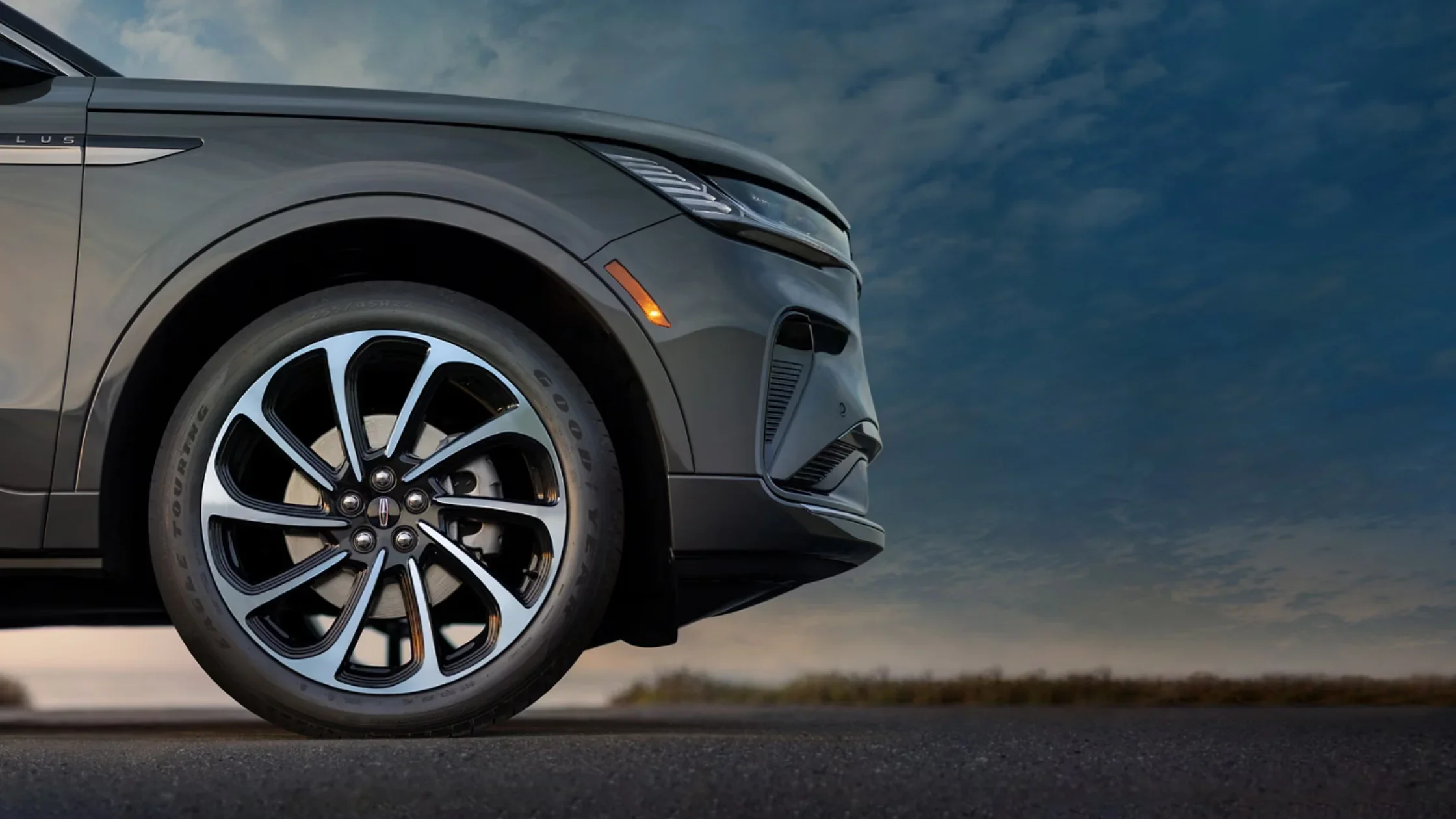 Close-up of Black Label Nautilus front wheel, headlamp, and grille at dusk under a dramatic sky.