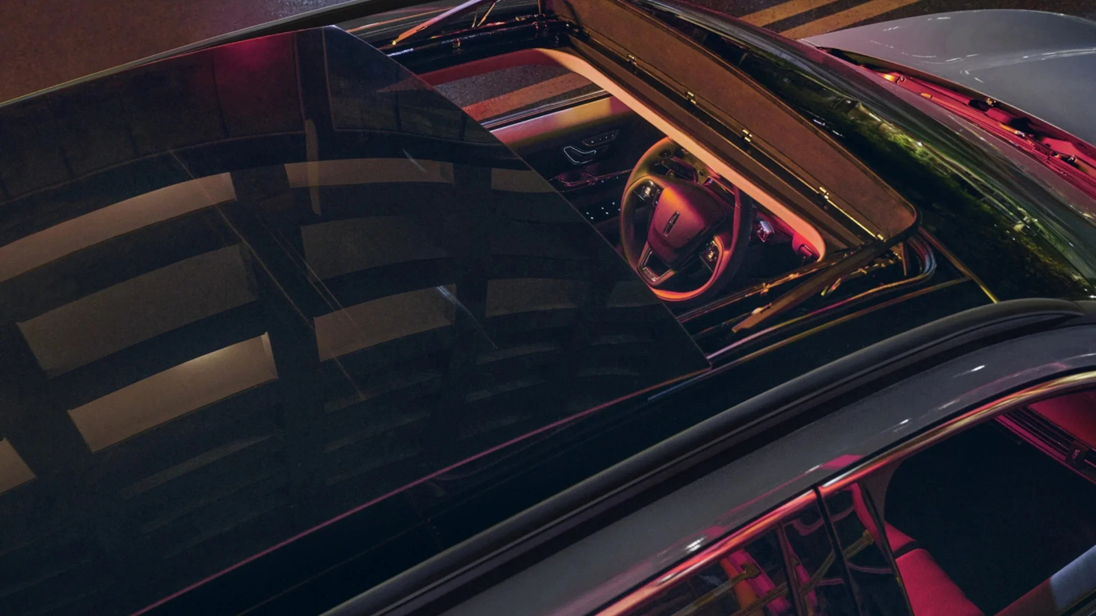 Top-down view through the panoramic sunroof of the 2025 Lincoln Corsair® Grand Touring, revealing ambient interior lighting and the front cabin design.