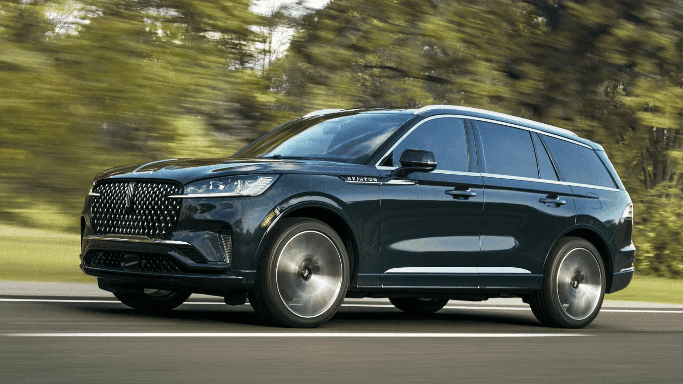 2025 Lincoln Aviator® in dark blue driving past blurred greenery on a smooth highway
