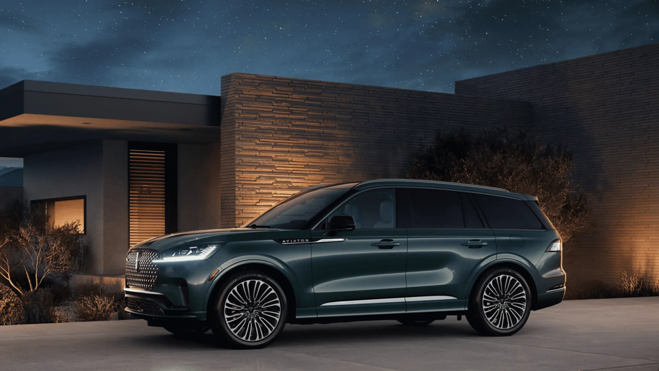 Side profile of 2025 Lincoln Aviator® in green parked in front of modern brick home at night
