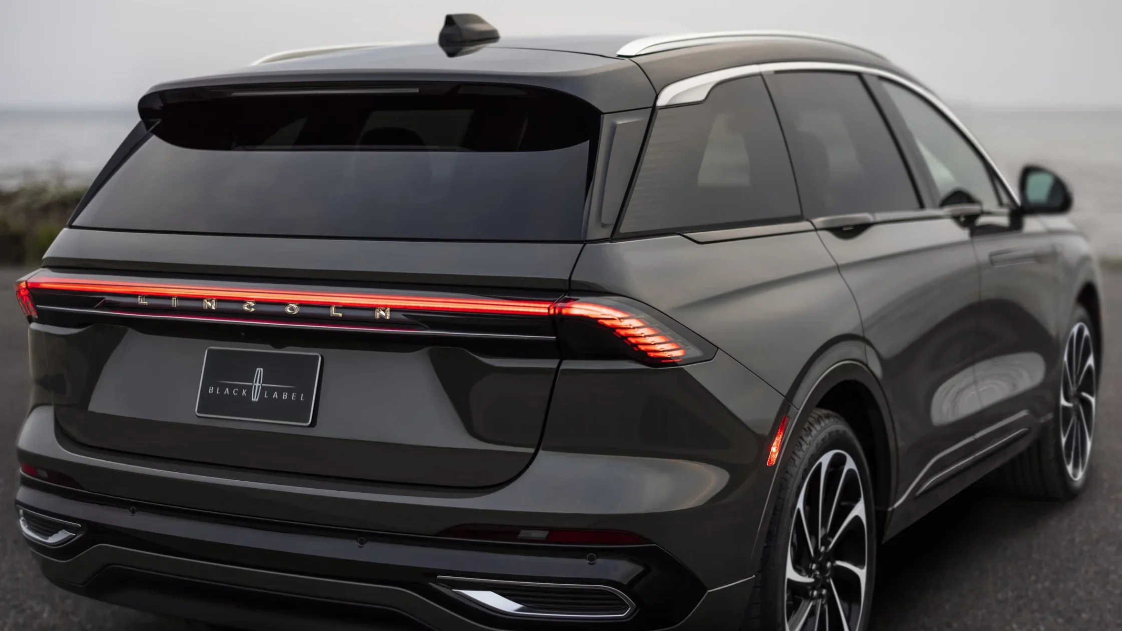 Rear view of the 2025 Lincoln Black Label Nautilus® parked by the coast, highlighting sleek taillights and polished rear badging.