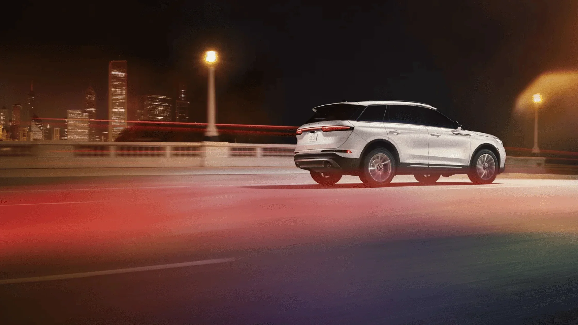 2025 Lincoln Corsair® in white driving across bridge at night with city skyline in the background