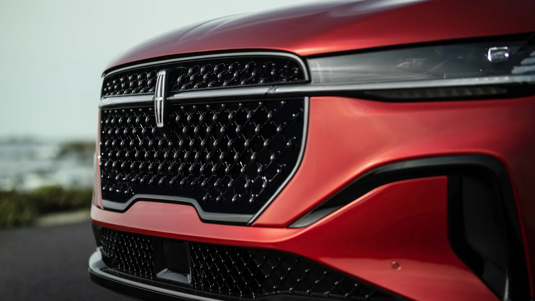 Wide-angle front grille shot of 2025 Lincoln Nautilus® Reserve in red finish with black mesh and LED headlights.