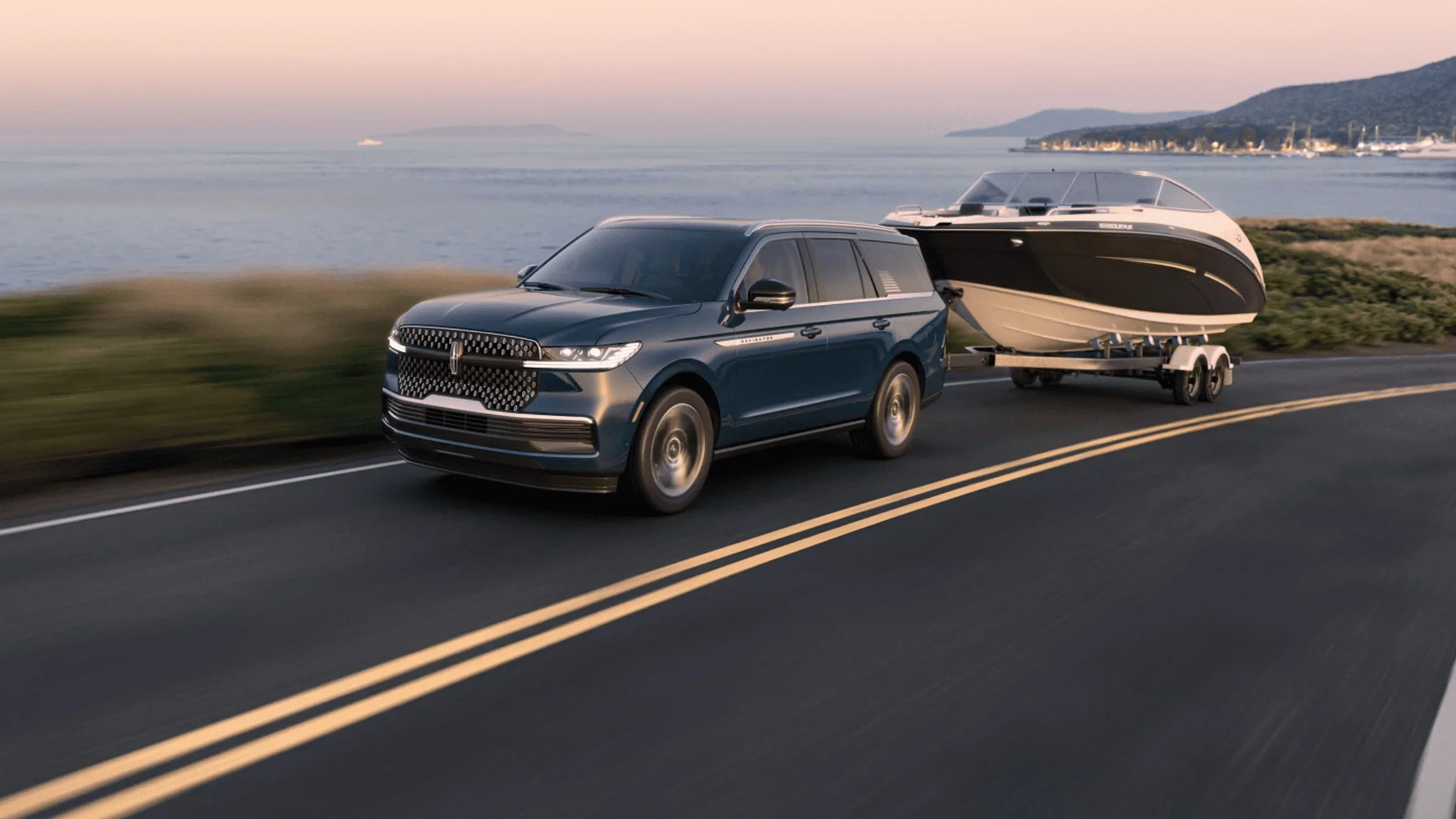 2025 Lincoln Navigator towing a luxury boat on a coastal road at sunset