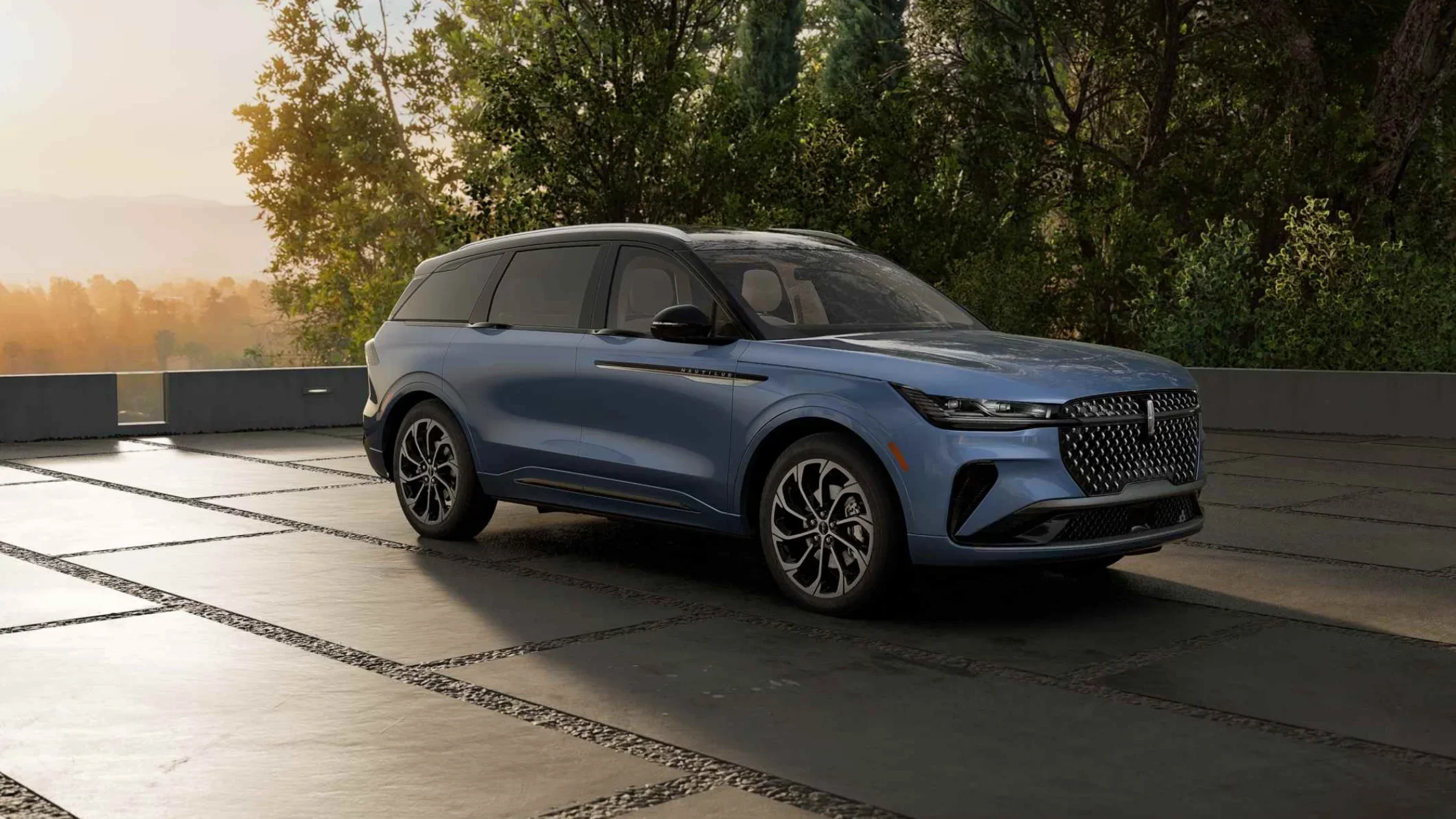 Side profile of gray 2025 Lincoln Nautilus driving through the desert with rock formations in the distance.