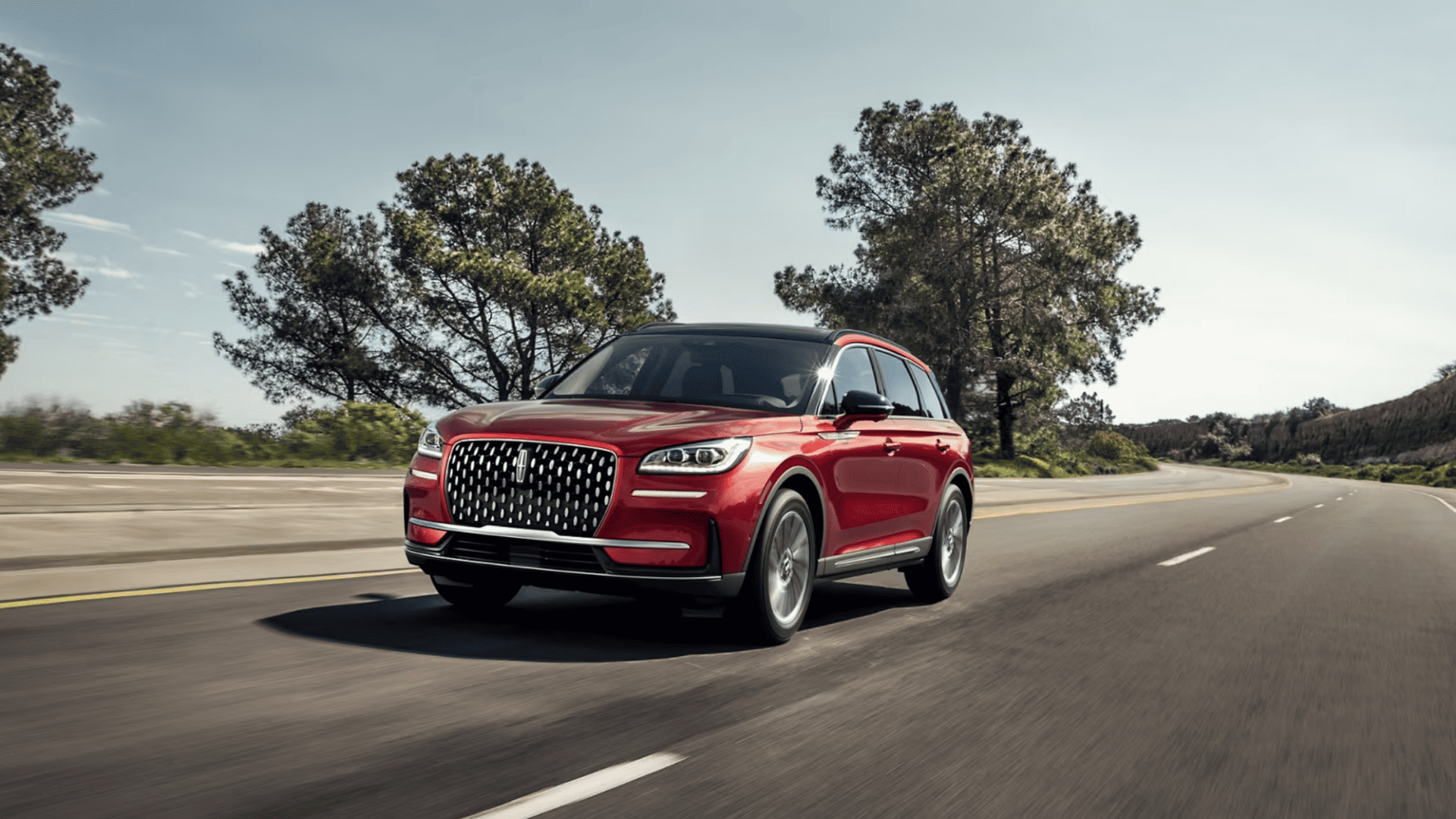 2025 Lincoln Corsair® Reserve driving on open road with red exterior, signature Lincoln grille, and LED headlights.