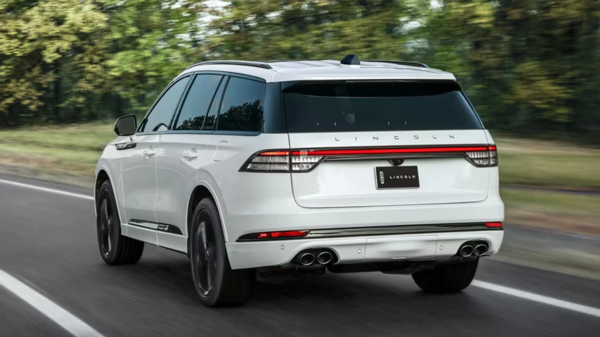 Rear view of a 2025 Aviator® Reserve driving on a tree-lined road, showcasing its modern LED light bar and quad exhaust design.