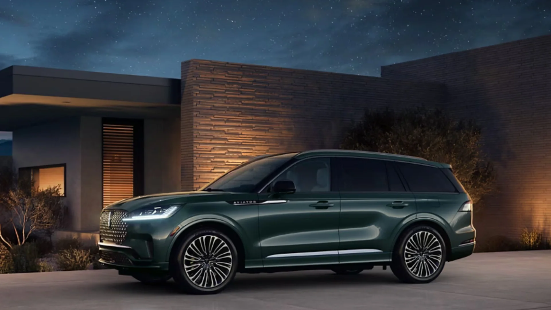 Front view of a 2025 Lincoln Aviator Reserve in green parked in front of a modern home at dusk.