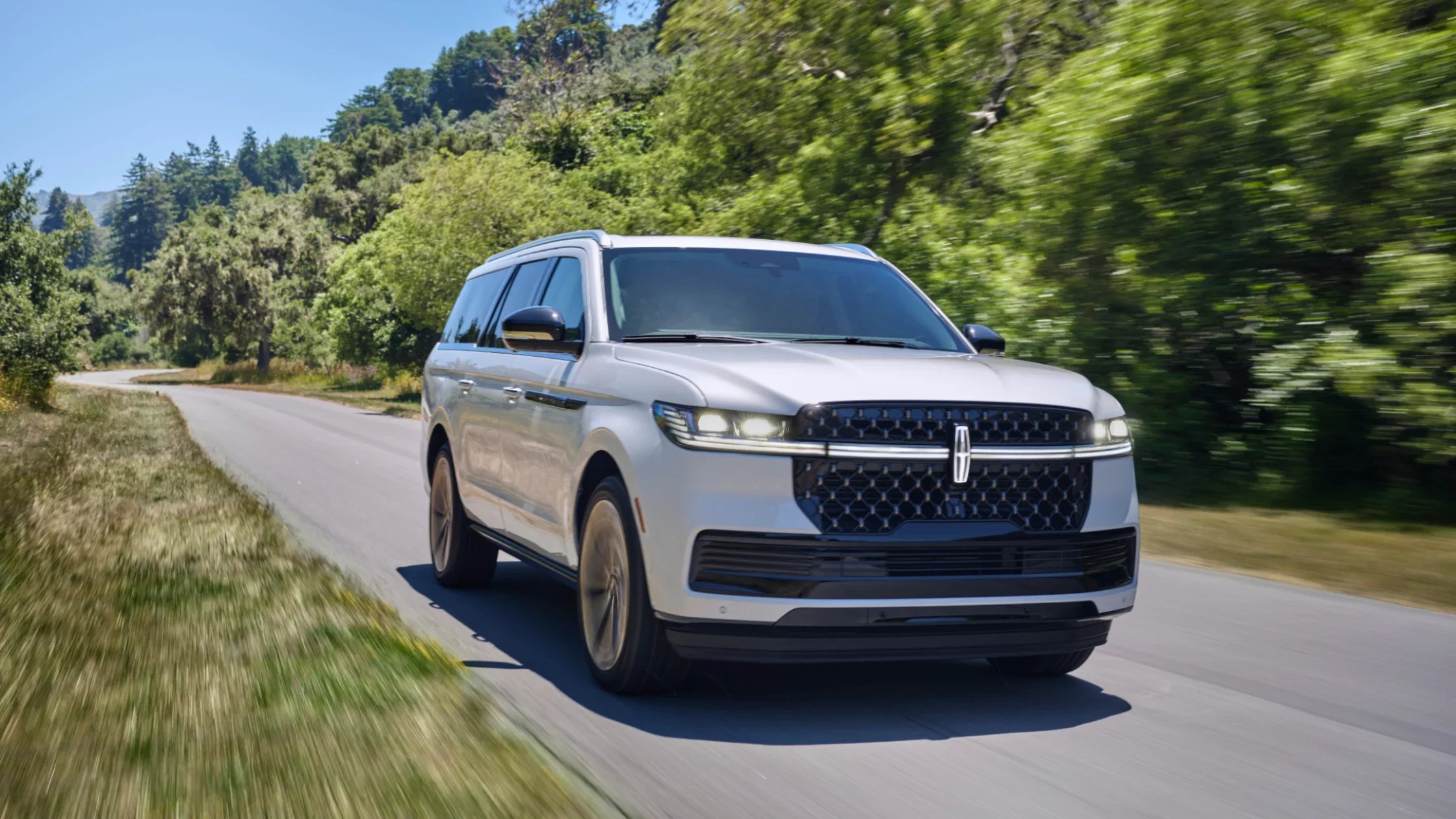 2025 Black Label Navigator® in motion on a tree-lined road, showcasing bold grille and sleek LED headlights.